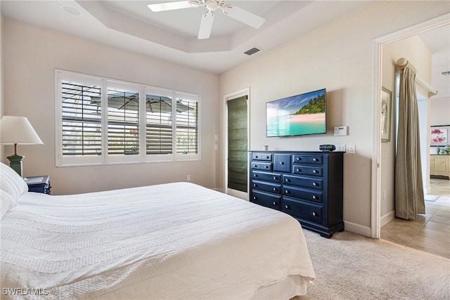 bedroom featuring a raised ceiling, ensuite bathroom, light carpet, and ceiling fan