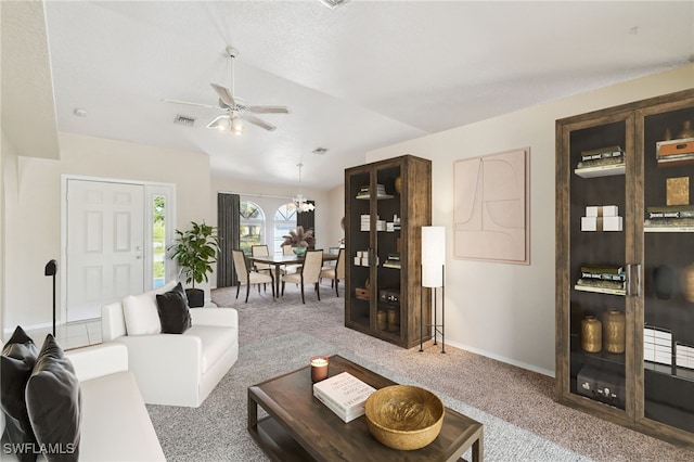 carpeted living room with ceiling fan with notable chandelier and vaulted ceiling