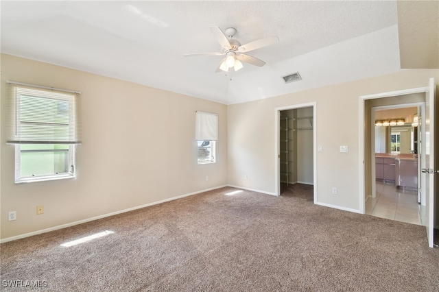 unfurnished bedroom featuring multiple windows, a walk in closet, light colored carpet, and ceiling fan