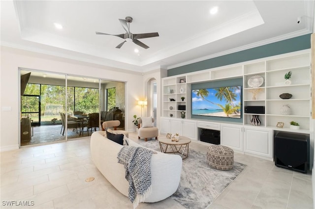 living room featuring built in shelves, light tile patterned flooring, ornamental molding, a raised ceiling, and ceiling fan