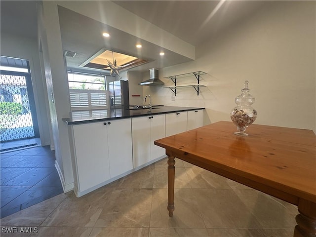 kitchen featuring a tray ceiling, sink, white cabinets, and wall chimney exhaust hood