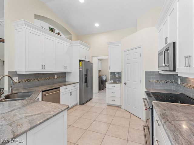 kitchen with washer and clothes dryer, light stone counters, appliances with stainless steel finishes, white cabinets, and a sink