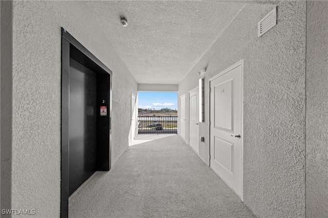 corridor featuring elevator, light colored carpet, and a textured ceiling