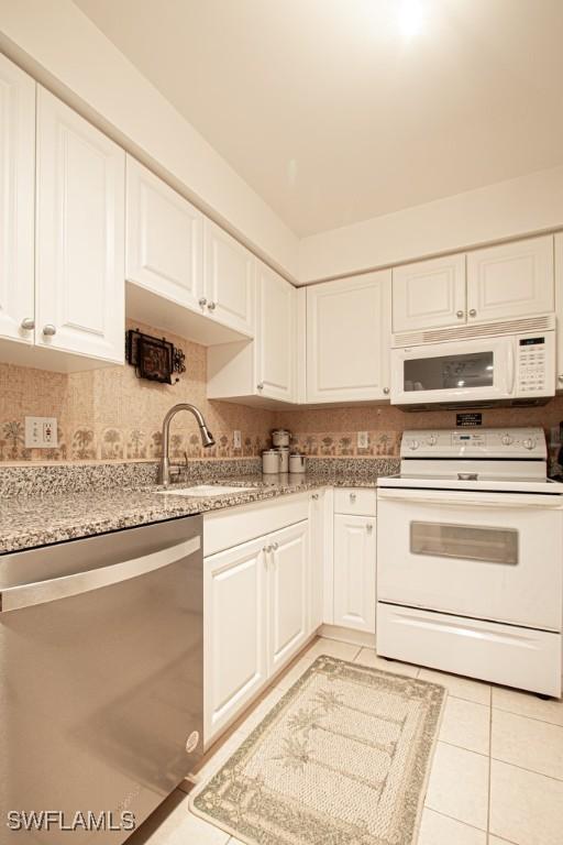 kitchen featuring sink, light stone counters, light tile patterned floors, white appliances, and white cabinets