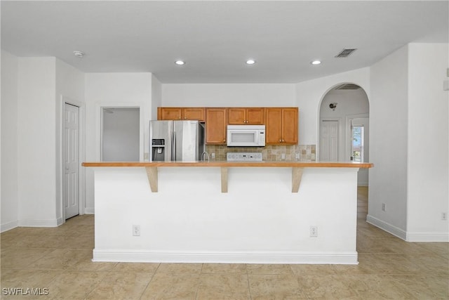 kitchen featuring tasteful backsplash, stainless steel fridge, a breakfast bar area, and an island with sink