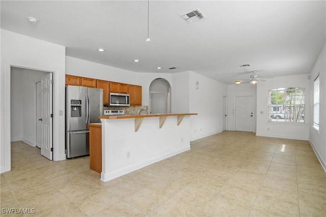 kitchen featuring an island with sink, backsplash, a kitchen breakfast bar, ceiling fan, and stainless steel appliances