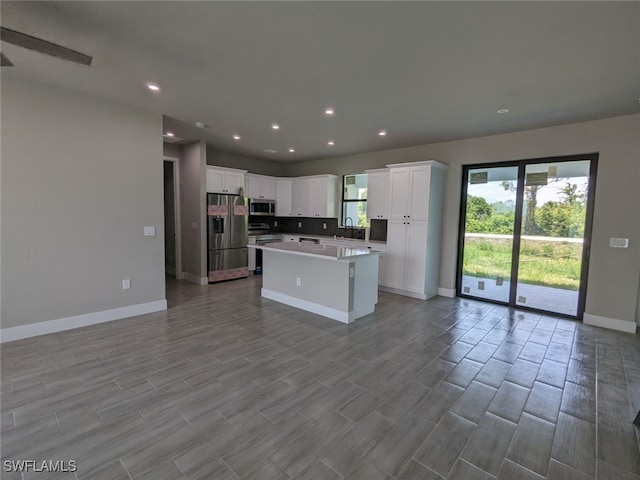 kitchen featuring a sink, stainless steel appliances, white cabinets, baseboards, and a kitchen island