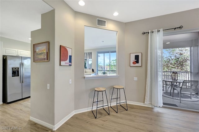 kitchen featuring white cabinetry, stainless steel fridge with ice dispenser, light hardwood / wood-style floors, and a kitchen breakfast bar