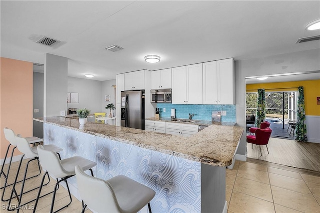 kitchen with white cabinetry, appliances with stainless steel finishes, a kitchen breakfast bar, and kitchen peninsula