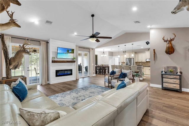 living room with ceiling fan with notable chandelier, vaulted ceiling, light hardwood / wood-style floors, and french doors