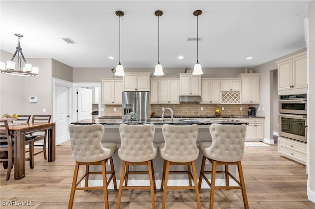 kitchen with pendant lighting, light hardwood / wood-style flooring, dark stone countertops, stainless steel appliances, and a center island with sink