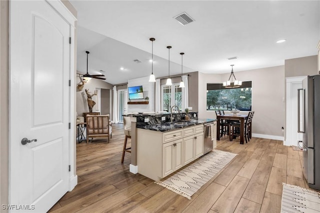 kitchen with appliances with stainless steel finishes, sink, dark stone countertops, a kitchen breakfast bar, and cream cabinets