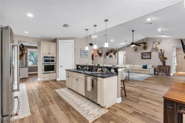 kitchen with decorative light fixtures, appliances with stainless steel finishes, a kitchen breakfast bar, dark stone counters, and cream cabinets