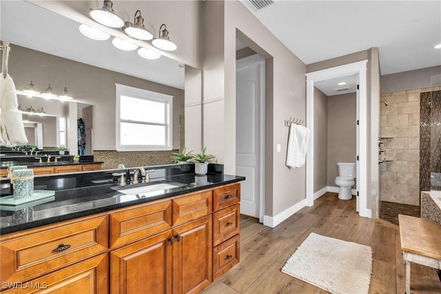 bathroom with hardwood / wood-style flooring, vanity, a tile shower, and toilet