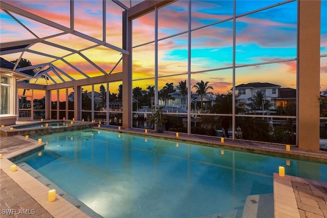 pool at dusk with an in ground hot tub, glass enclosure, and a patio area