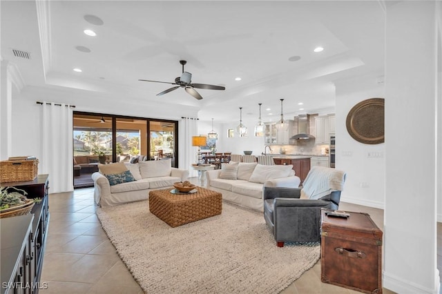 living room featuring light tile patterned flooring, ceiling fan, and a tray ceiling