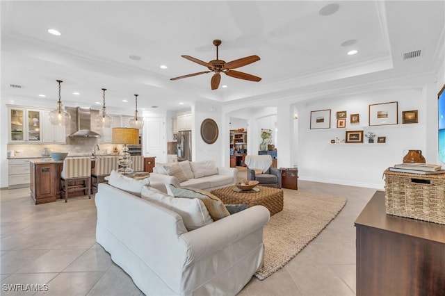 tiled living room with a tray ceiling, ornamental molding, and ceiling fan