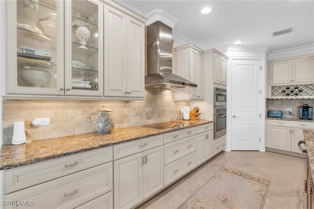 kitchen with light stone counters, black electric cooktop, double oven, wall chimney range hood, and white cabinets