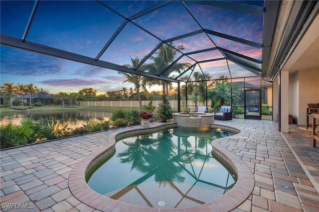 pool at dusk featuring an in ground hot tub, a water view, glass enclosure, and a patio