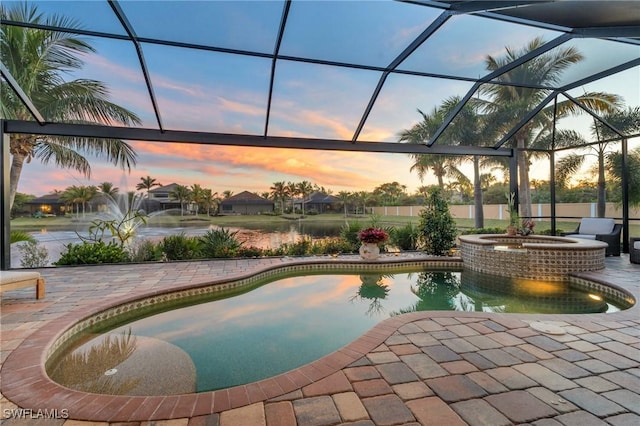 pool at dusk with an in ground hot tub, glass enclosure, and a patio