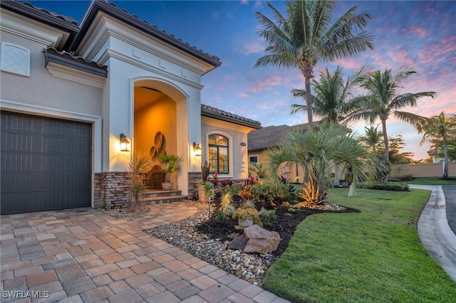 exterior entry at dusk with a garage and a lawn