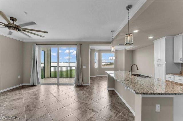 kitchen featuring stone countertops, pendant lighting, sink, white cabinets, and a center island with sink