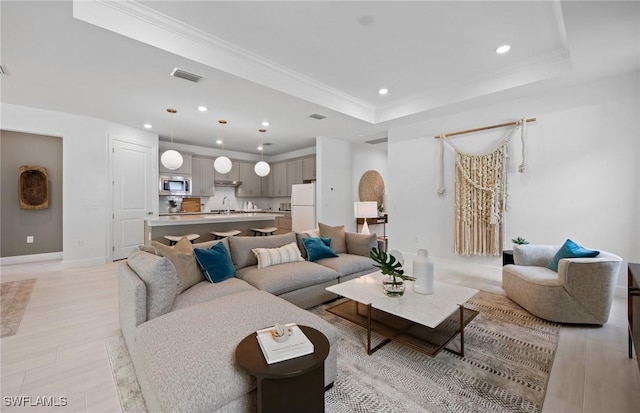 living room with crown molding, sink, and a tray ceiling