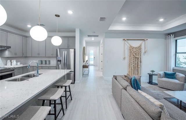 kitchen with sink, gray cabinets, stainless steel appliances, light stone counters, and decorative light fixtures