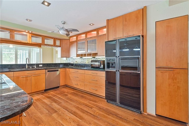 kitchen with sink, black fridge, light wood-type flooring, stainless steel dishwasher, and dark stone counters