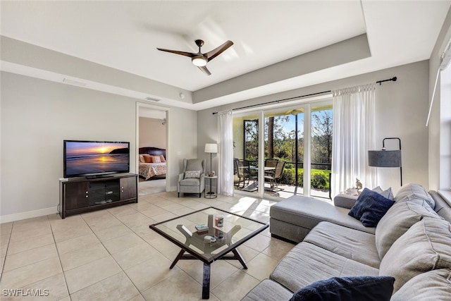 tiled living room with ceiling fan and a tray ceiling