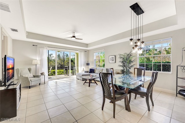 tiled dining space with a raised ceiling and ceiling fan with notable chandelier