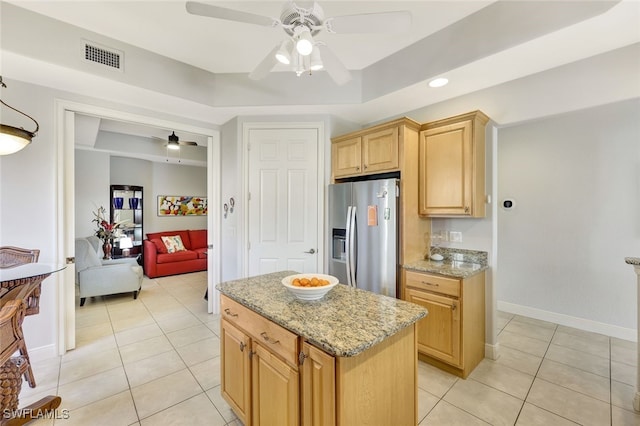 kitchen with stainless steel fridge, ceiling fan, light stone countertops, a kitchen island, and a raised ceiling