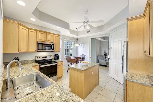 kitchen featuring light brown cabinets, a sink, a tray ceiling, a center island, and appliances with stainless steel finishes