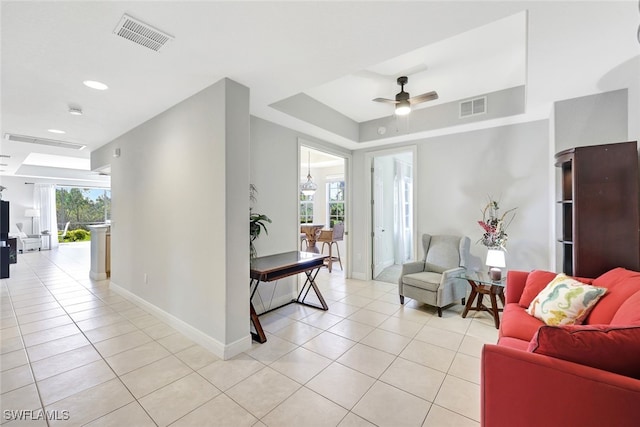 tiled living room with ceiling fan, plenty of natural light, and a raised ceiling