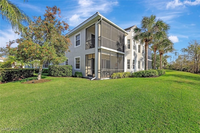 back of property with a yard, stucco siding, and a sunroom