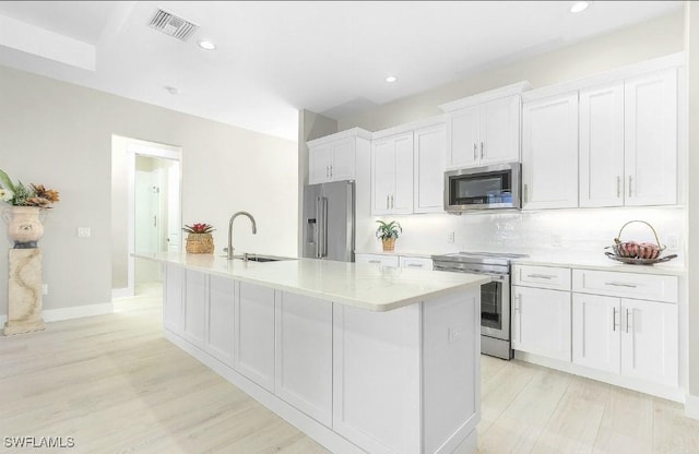 kitchen with sink, white cabinets, a kitchen island with sink, light hardwood / wood-style floors, and stainless steel appliances