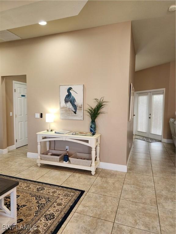 corridor with light tile patterned flooring, a towering ceiling, and french doors