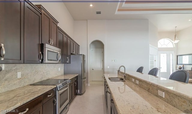 kitchen with pendant lighting, a breakfast bar area, appliances with stainless steel finishes, a sink, and light stone countertops