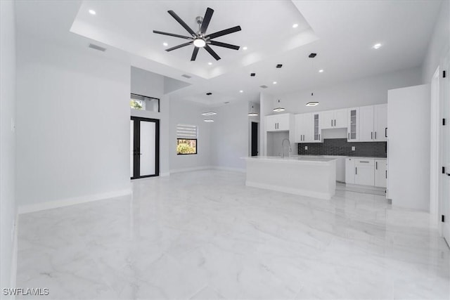 living room featuring ceiling fan, a towering ceiling, a tray ceiling, and sink