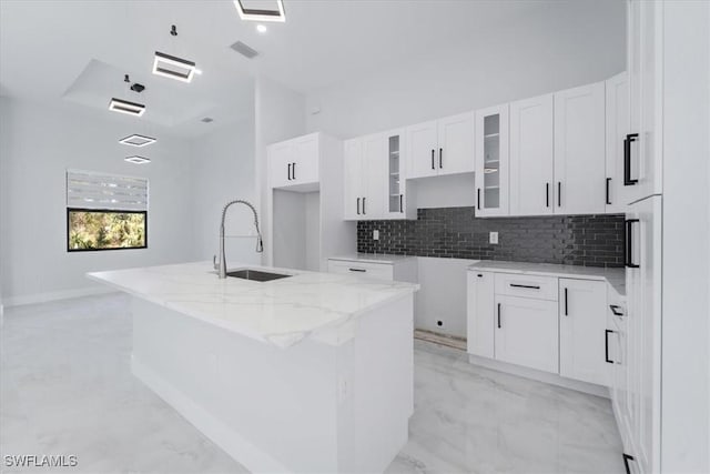 kitchen with sink, light stone counters, white cabinets, a kitchen island with sink, and backsplash