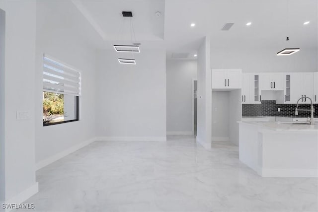 kitchen with white cabinetry, backsplash, a high ceiling, a tray ceiling, and light stone countertops