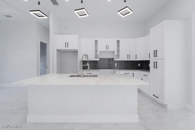 kitchen featuring sink, white cabinetry, tasteful backsplash, light stone countertops, and an island with sink