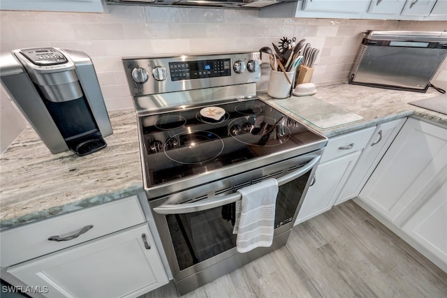 kitchen with white cabinetry, decorative backsplash, light stone counters, light wood-type flooring, and electric stove