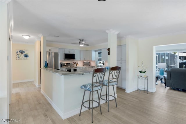 kitchen with stainless steel appliances, ornamental molding, kitchen peninsula, and ornate columns