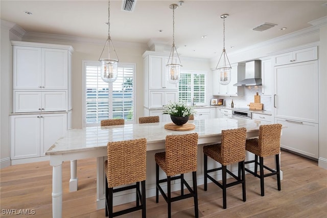 kitchen featuring a large island, wall chimney range hood, a breakfast bar, white cabinetry, and hanging light fixtures