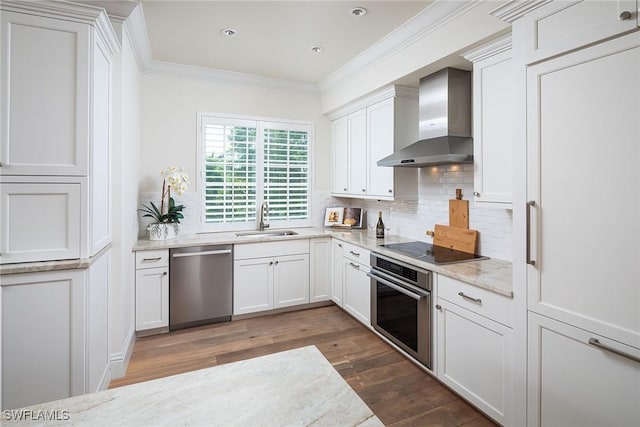 kitchen with appliances with stainless steel finishes, sink, white cabinets, ornamental molding, and wall chimney exhaust hood