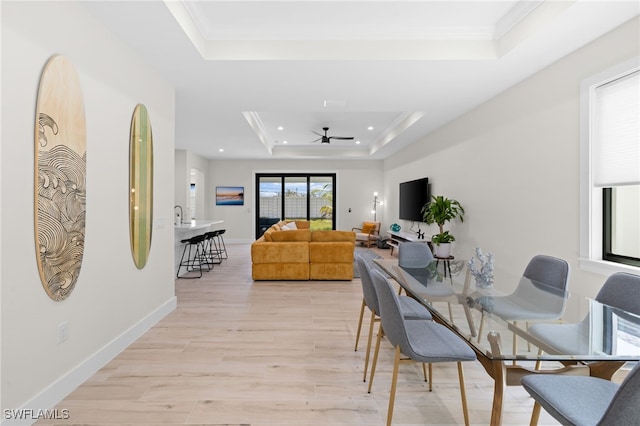 dining room with ornamental molding, ceiling fan, light wood-type flooring, and a tray ceiling