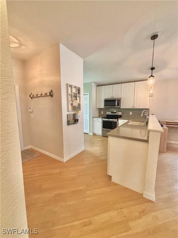 kitchen featuring sink, white cabinetry, decorative light fixtures, kitchen peninsula, and stainless steel appliances