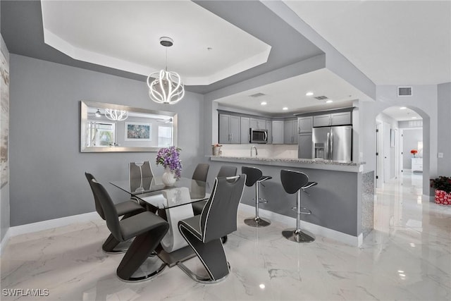 dining room with a raised ceiling, sink, and an inviting chandelier