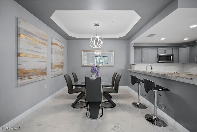 dining area featuring an inviting chandelier, a raised ceiling, and sink